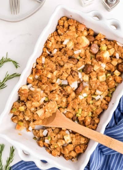 Thanksgiving stuffing in a white dish with a wooden spoon.