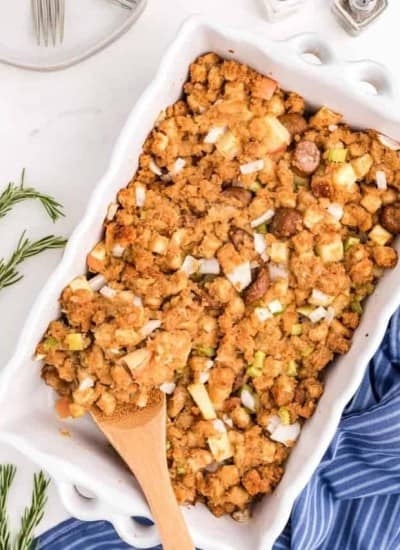 sausage apple Stuffing in a white dish with a wooden spoon.