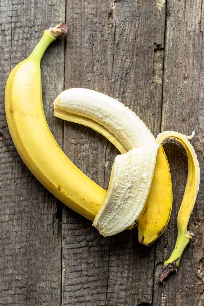 Ripe bananas on wooden table with one being peeled