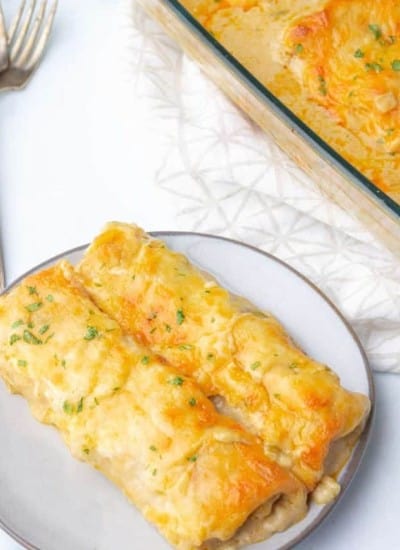 Creamy White Chicken Enchiladas - Cheesy enchiladas on a plate with a fork.