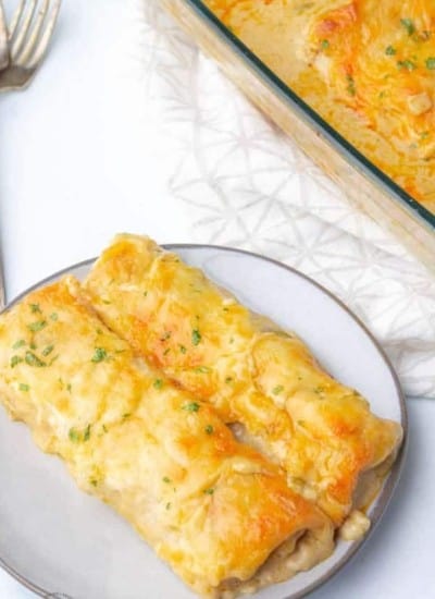 Cheesy chicken enchiladas on a plate with a fork.