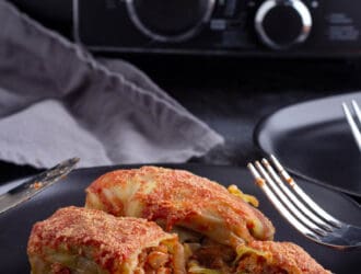 Crock pot stuffed cabbage rolls recipe cooked set on a black plate with a fork and knife