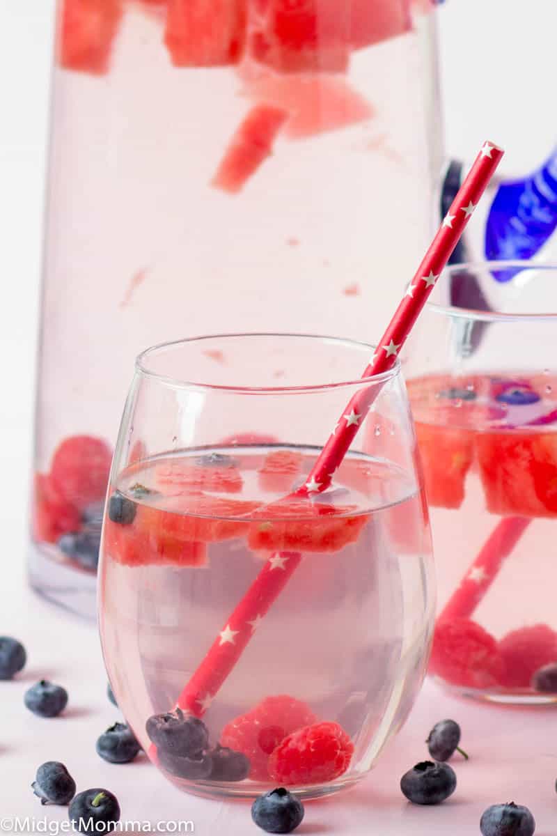 Fruit Infused water with raspberries, blueberries and raspberries in a glass pitcher with a glass of water poured next to it