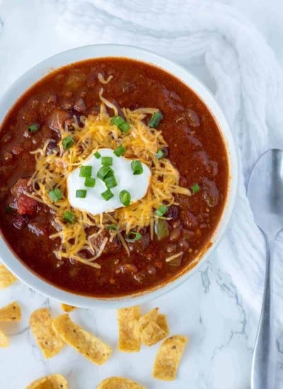 How to make crockpot chili low carb - chili in a bowl on the counter topped with green onions, cheddar cheese and sour cream