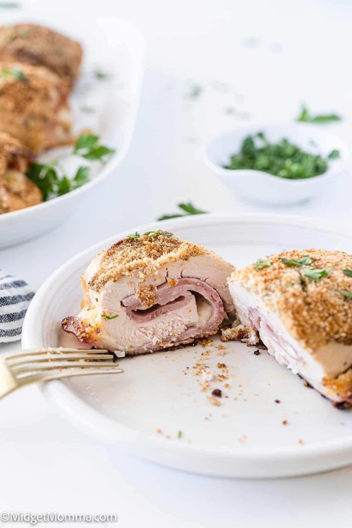 stuffed chicken with cheese and ham cut in half on a white plate with a fork