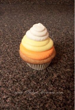 3rd step for making candy corn cupcakes - the white frosting swirl on top of the yellow and orange frosting swirls