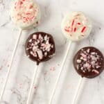 2 white chocolate covered oreos and 2 milk chocolate covered oreos with crushed up candy canes on top of them on a lolipop stick