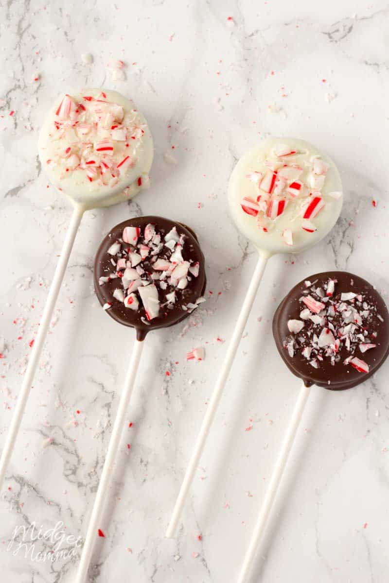 2 white chocolate covered oreos and 2 milk chocolate covered oreos with crushed up candy canes on top of them on a lolipop stick