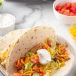 Open chicken taco in soft taco shell with lettuce, tomato, cheese and sour cream
