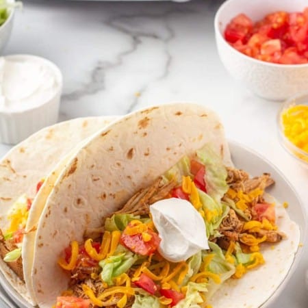 Open chicken taco in soft taco shell with lettuce, tomato, cheese and sour cream