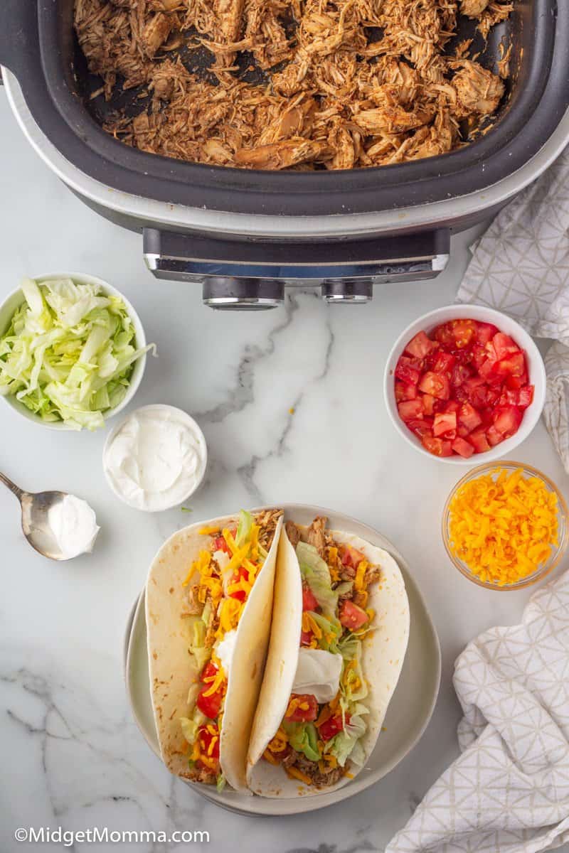 Slow Cooker Chicken Tacos on a plaate, chicken taco meat iin the slow cooker and taco toppings in bowls