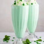 2 Mint milkshakes in clear glasses topped with whipped cream and a cherry