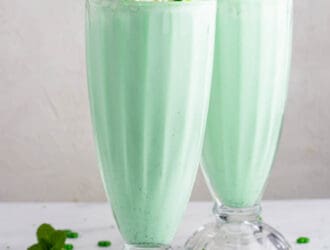 2 Mint milkshakes in clear glasses topped with whipped cream and a cherry