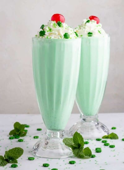 2 Mint milkshakes in clear glasses topped with whipped cream and a cherry