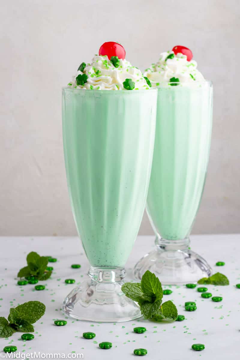 2 Mint milkshakes in clear glasses topped with whipped cream and a cherry