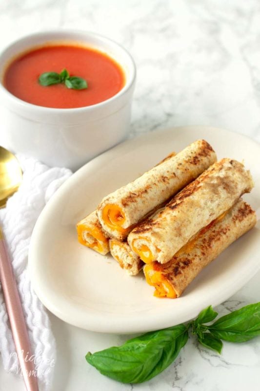 Grilled Cheese Roll Ups on a white plate with a bowl of fresh homemade tomato soup