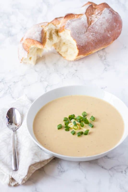 crockpot Cauliflower and Cheese soup in a white bowl with a spoon and a piece of bread
