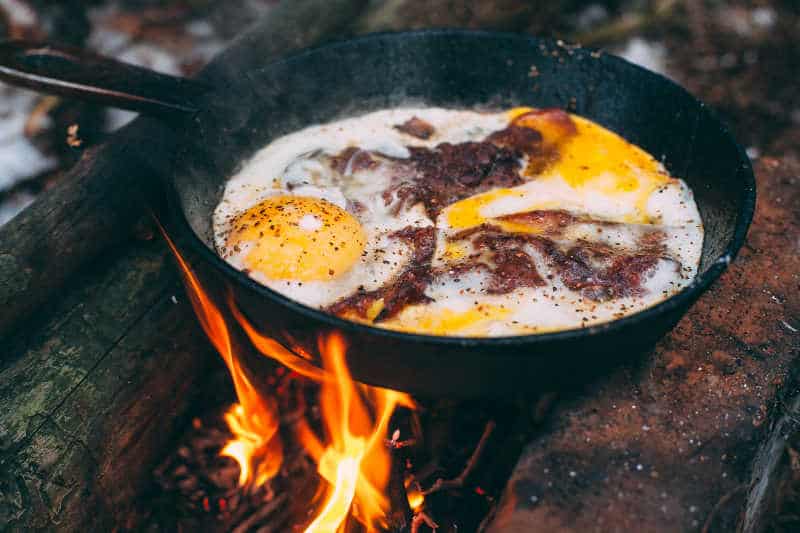 Fried eggs with bacon in a pan in the forest. Food at the camp. Fried egg with bacon on fire. Picnic