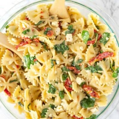 Sun Dried tomato Pasta Salad in a glass bowl with a wooden spoon