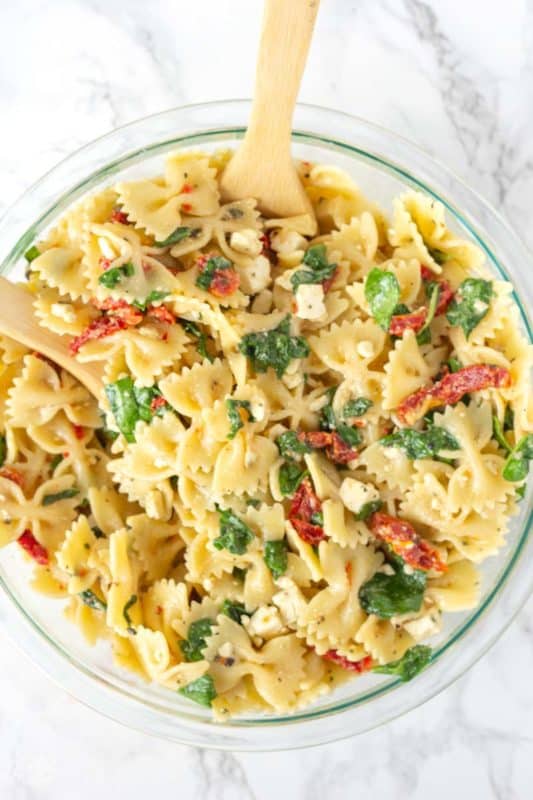 Sun Dried tomato Pasta Salad in a glass bowl with a wooden spoon