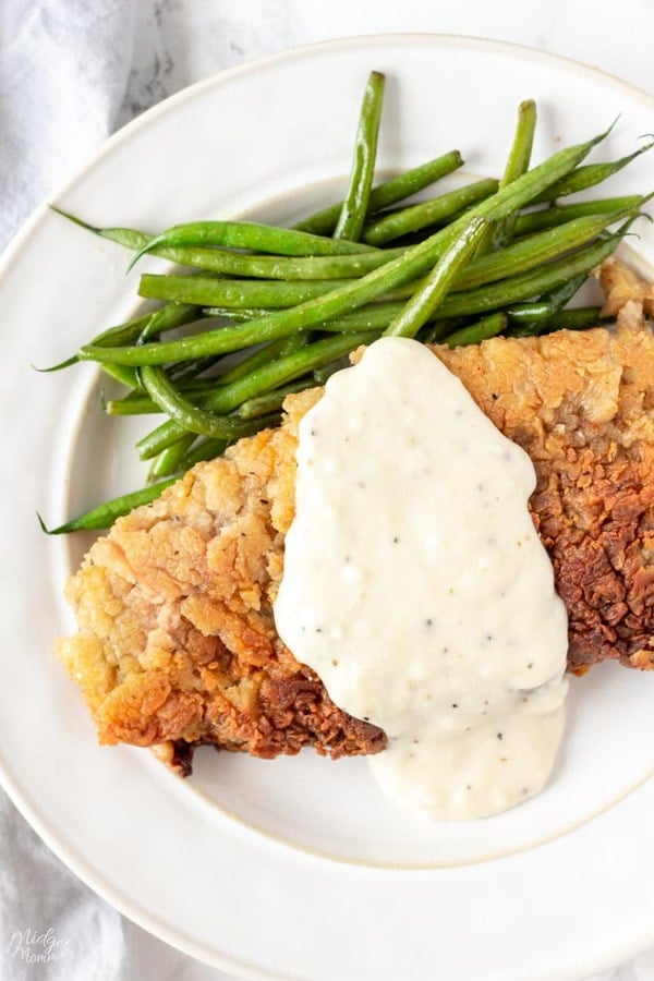 Chicken Fried Steak covered with white gravy on a white plate with green beans