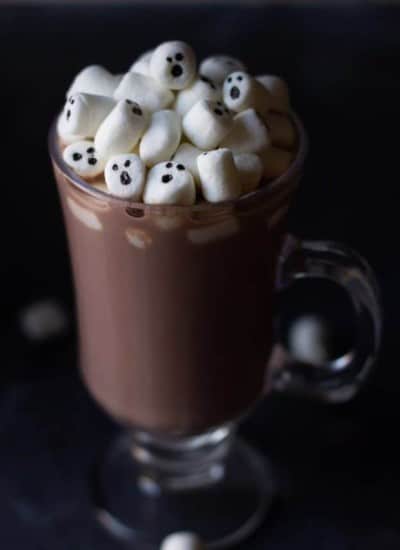 Homemade hot chocolate in a clear mug with marshmallows on top with ghosts faces on them