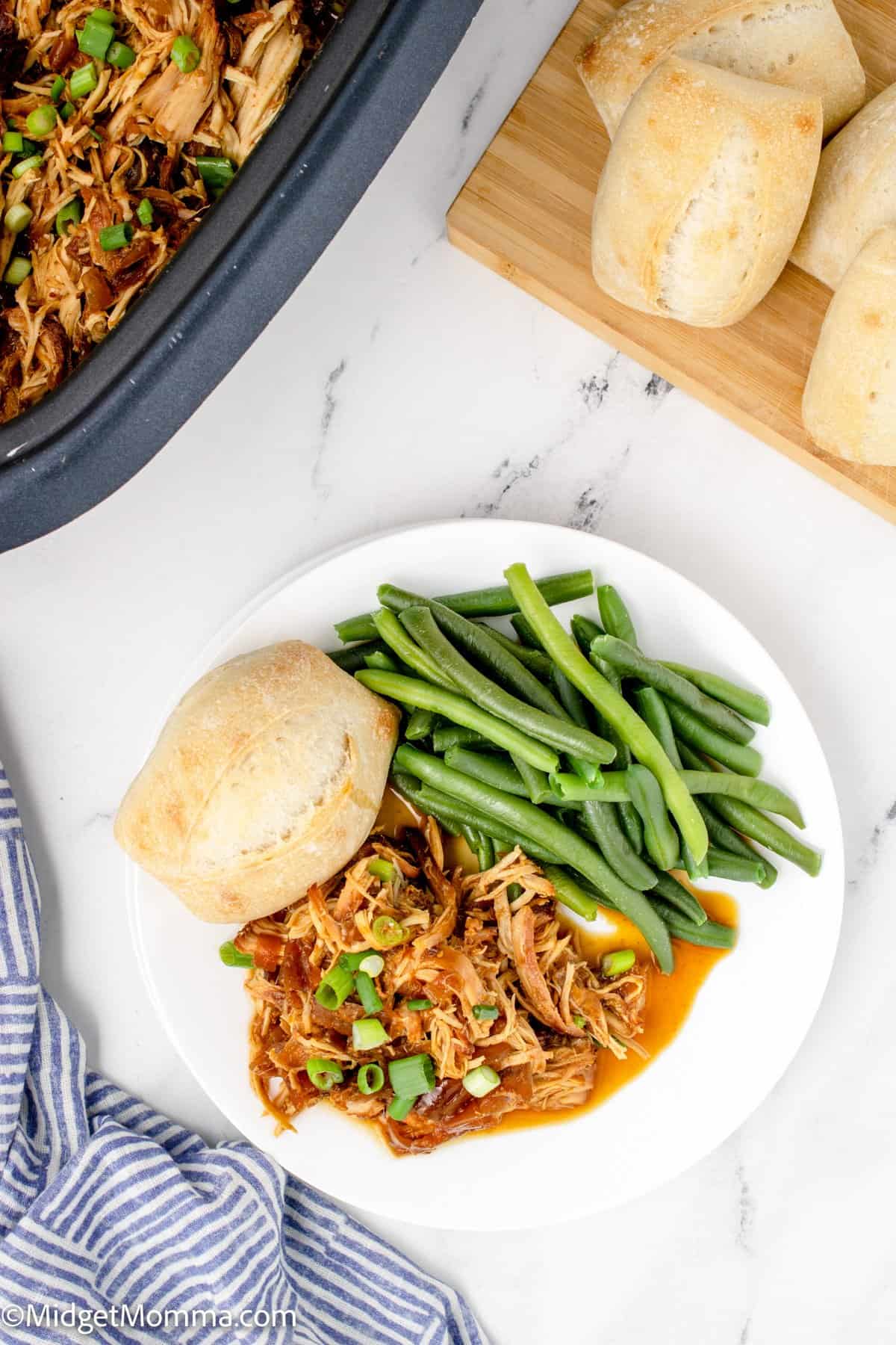 overhead photo of Slow Cooker Honey Garlic Chicken on a plate served with green beans and a roll.