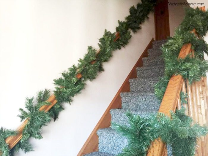 Evergreen garland wrapped around wooden handrail going up a staircase.