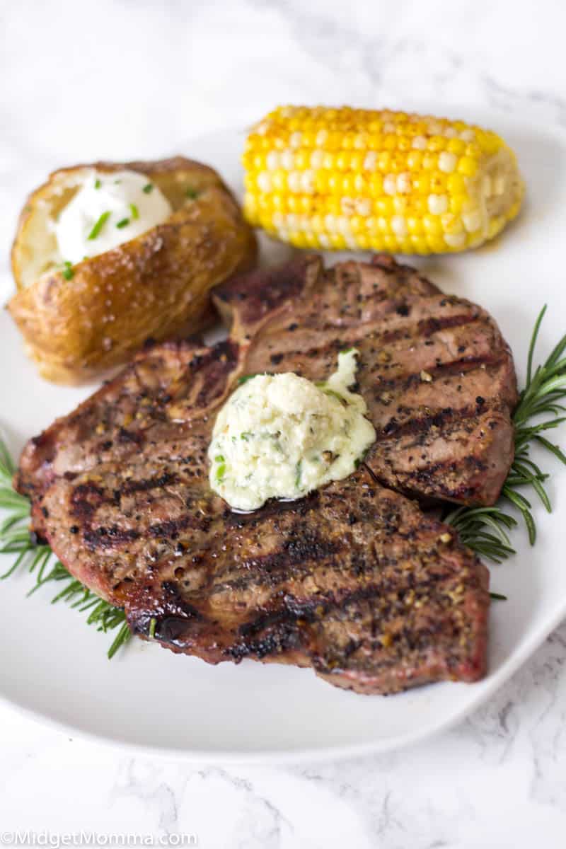 Grilled steak with a baked potato and corn on the cob on a white plate