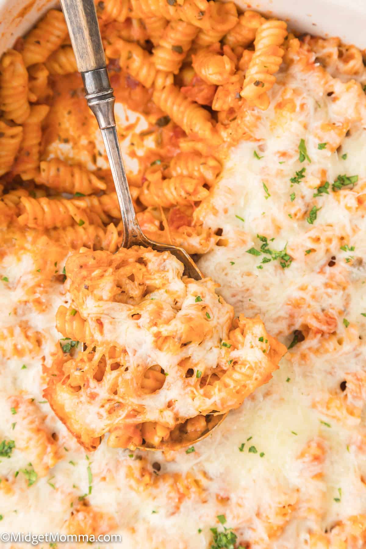 A dish of baked pink sauce pasta bake topped with melted cheese and a serving fork lifting a portion.