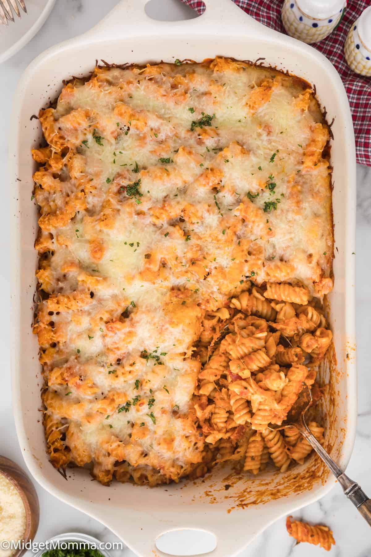Baked pasta casserole made with alfredo sauce and tomato sauce with a golden cheese topping in a white dish, partially served.
