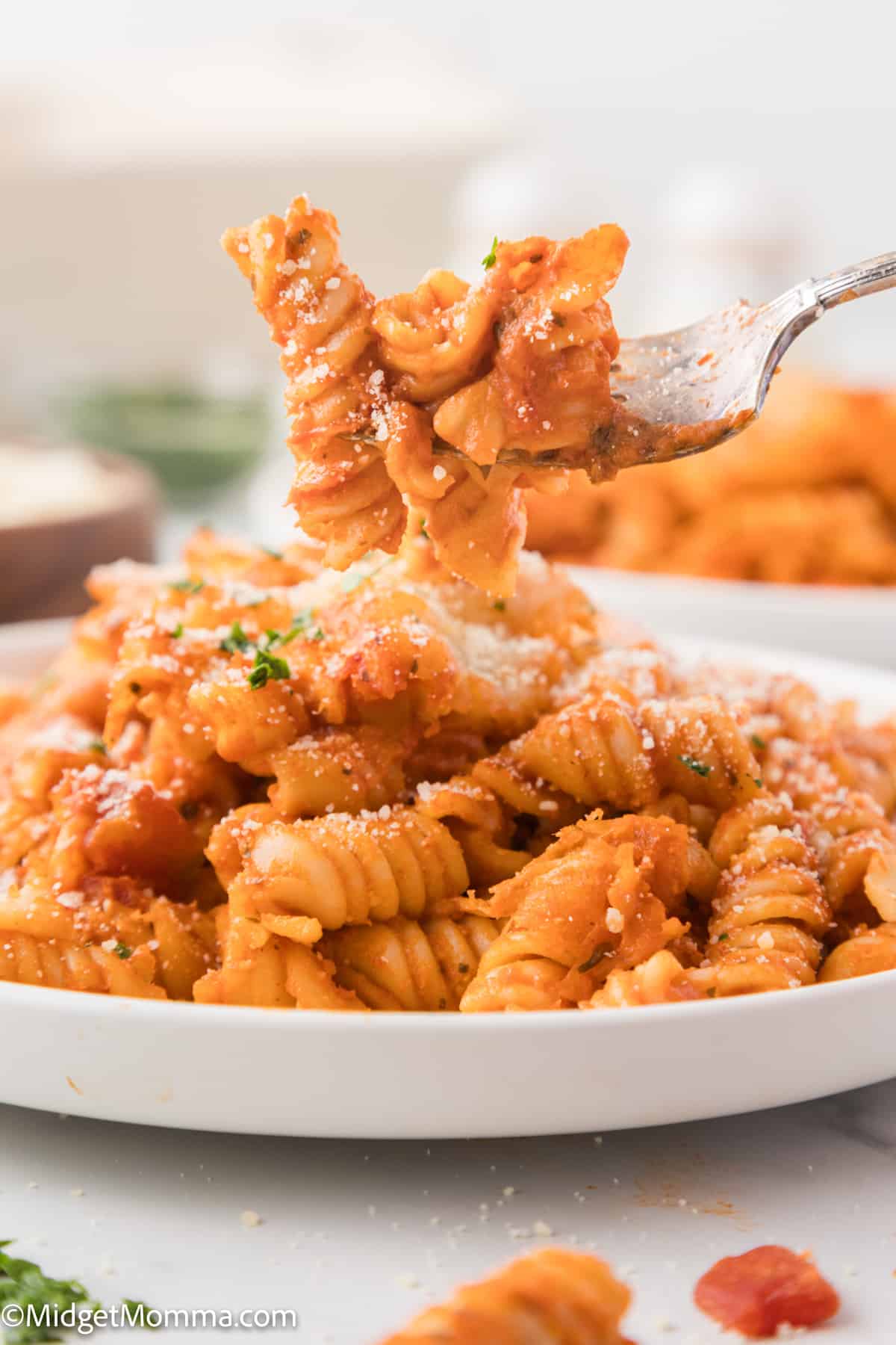 A fork lifting a portion of rotini pasta coated in tomato sauce and sprinkled with parmesan cheese.