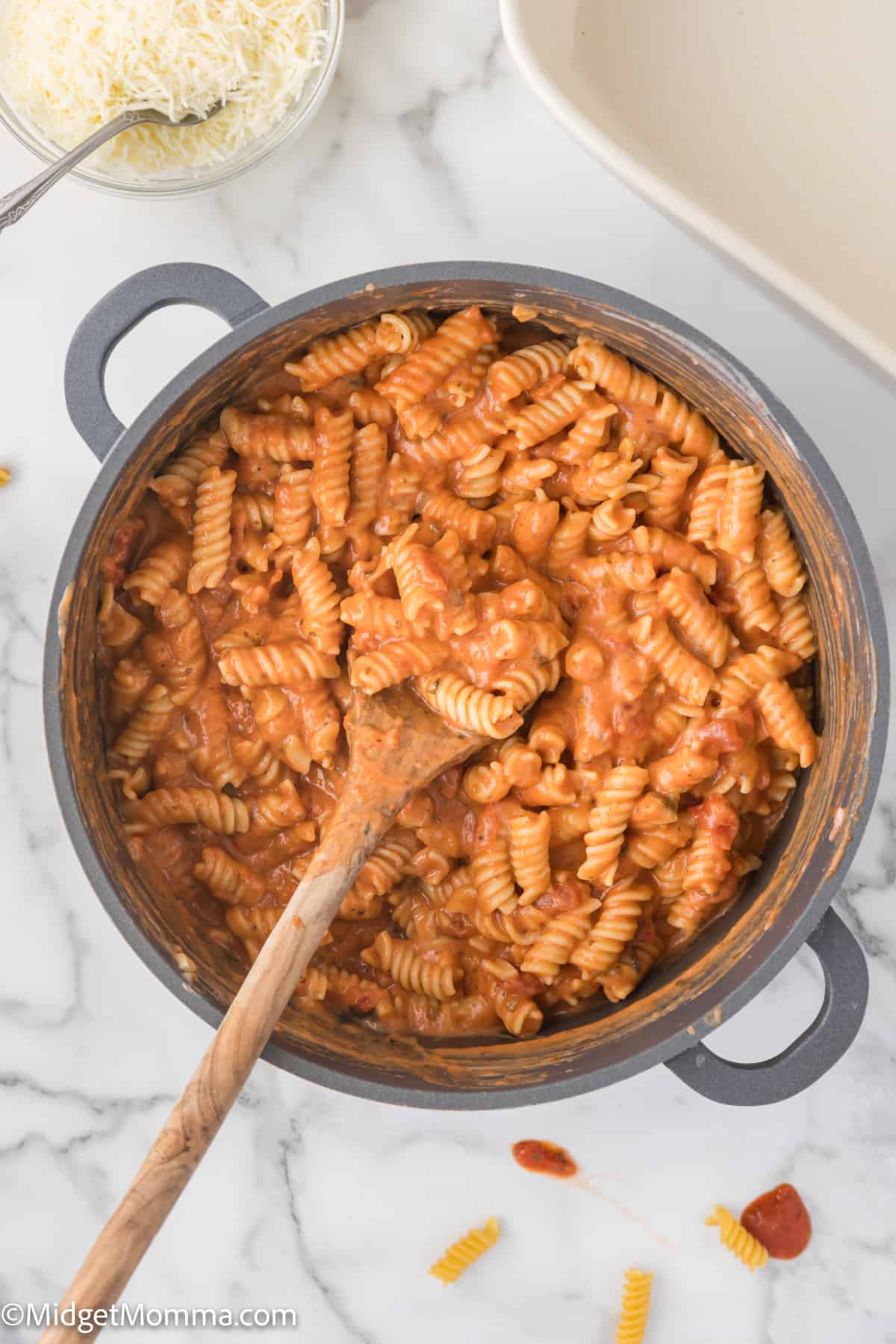 A pot of marinara alfredo sauce mixed with pasta  with a wooden spoon on a marble countertop.