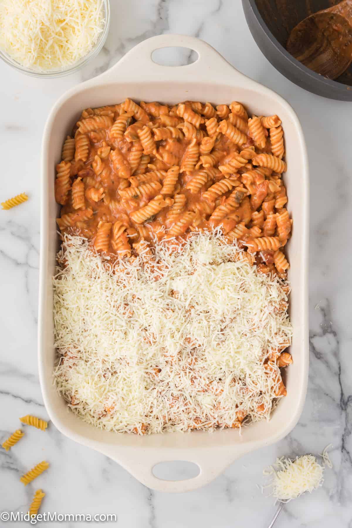 Baked pasta dish topped with shredded mozzarella cheese in a white ceramic baking dish.