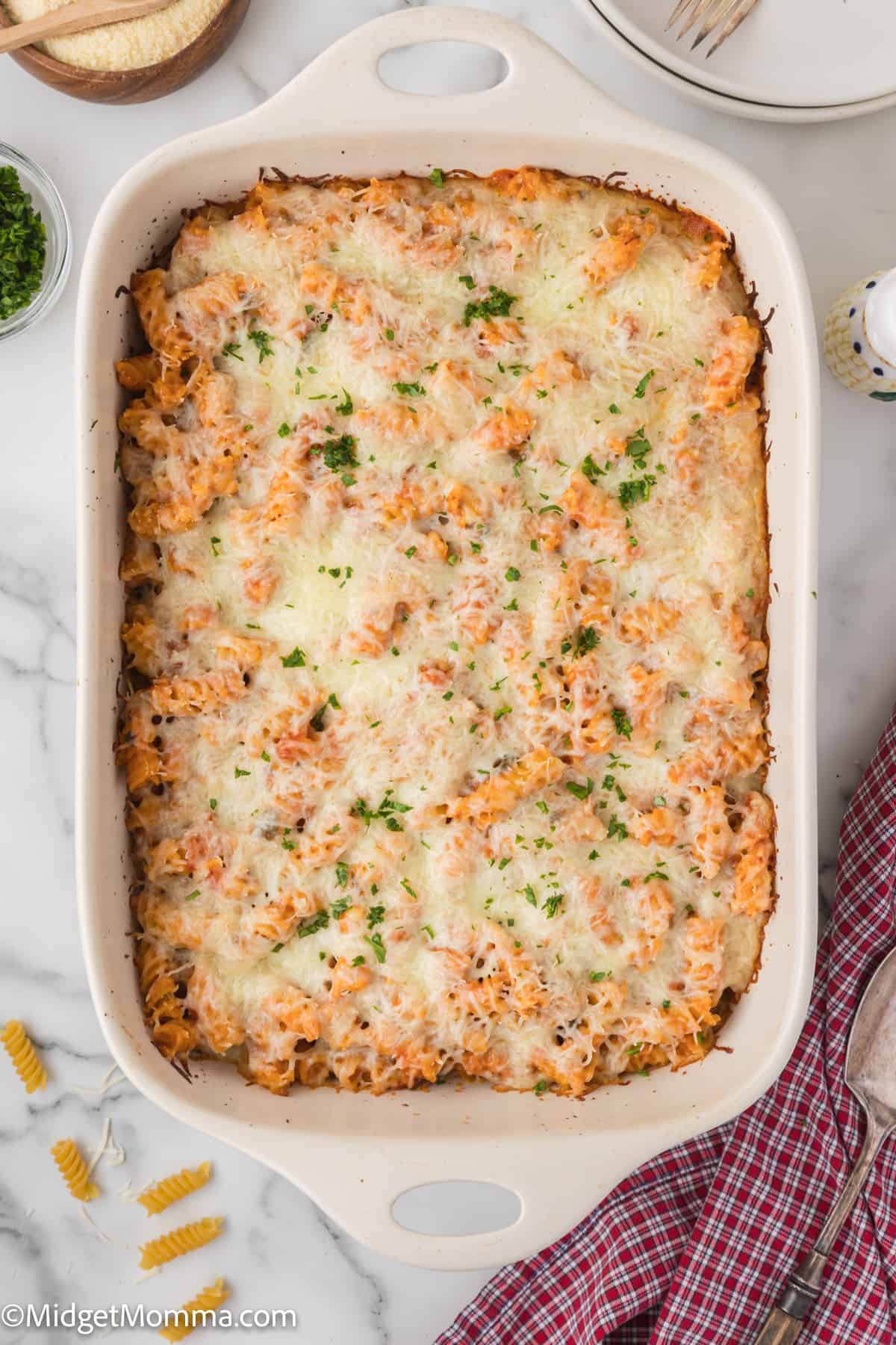 A homemade pink sauce pasta casserole topped with melted mozzarella cheese and garnished with herbs in a white baking dish.