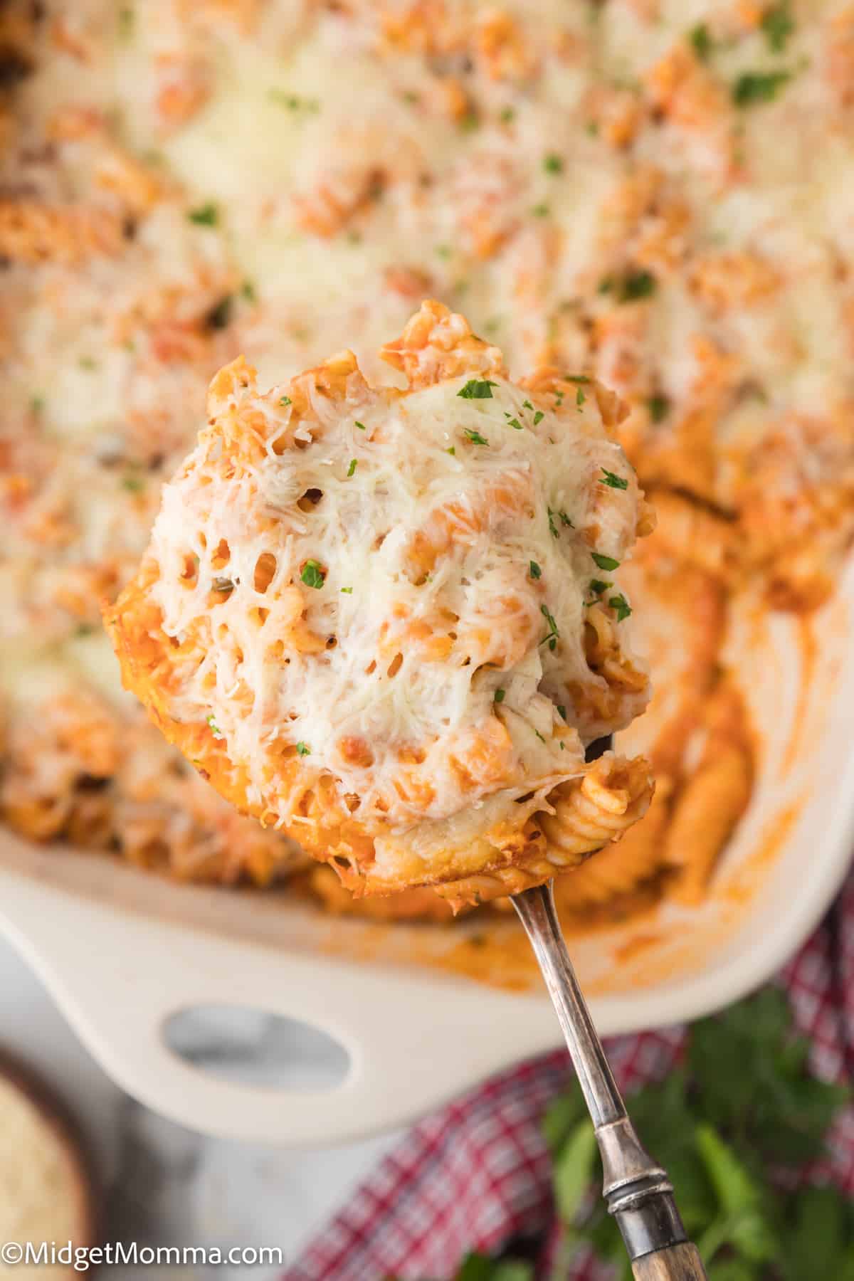 Spoon serving a portion of baked cheesy pasta casserole, with melted cheese on top.