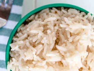 easy garlic rice in a green bowl with a fork and a blue and white cloth napkin