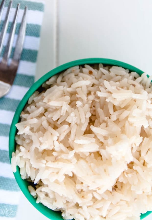 easy garlic rice in a green bowl with a fork and a blue and white cloth napkin
