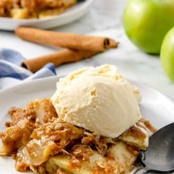 Apple crisp topped with ice cream on a plate with cinnamon sticks and apples