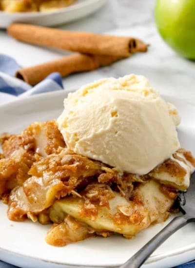 Apple crisp topped with ice cream on a plate with cinnamon sticks and apples