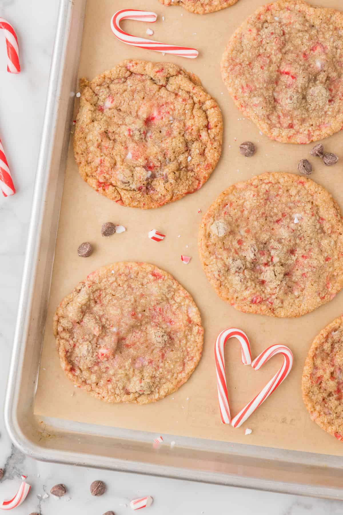Peppermint chocolate chip cookies on a baking sheet with candy canes.