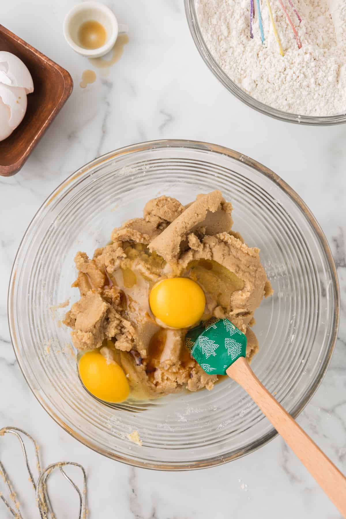 A bowl with eggs and cookie dough with a bowl of flour next to it.