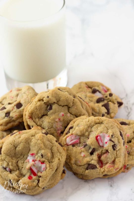 Chocolate chip cookies made with candy canes in a pile and a glass of milk.