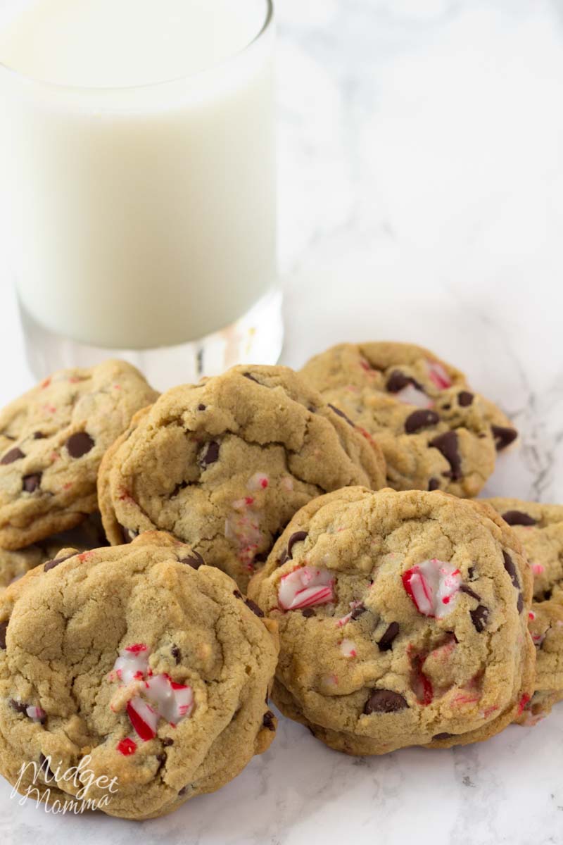 Chocolate chip cookies made with candy canes in a pile and a glass of milk.