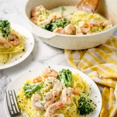 white plate with Shrimp Alfredo Spaghetti Squash with Broccoli and the serving dish with the rest of the meal in the background