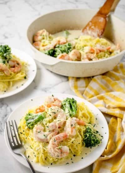 white plate with Shrimp Alfredo Spaghetti Squash with Broccoli and the serving dish with the rest of the meal in the background