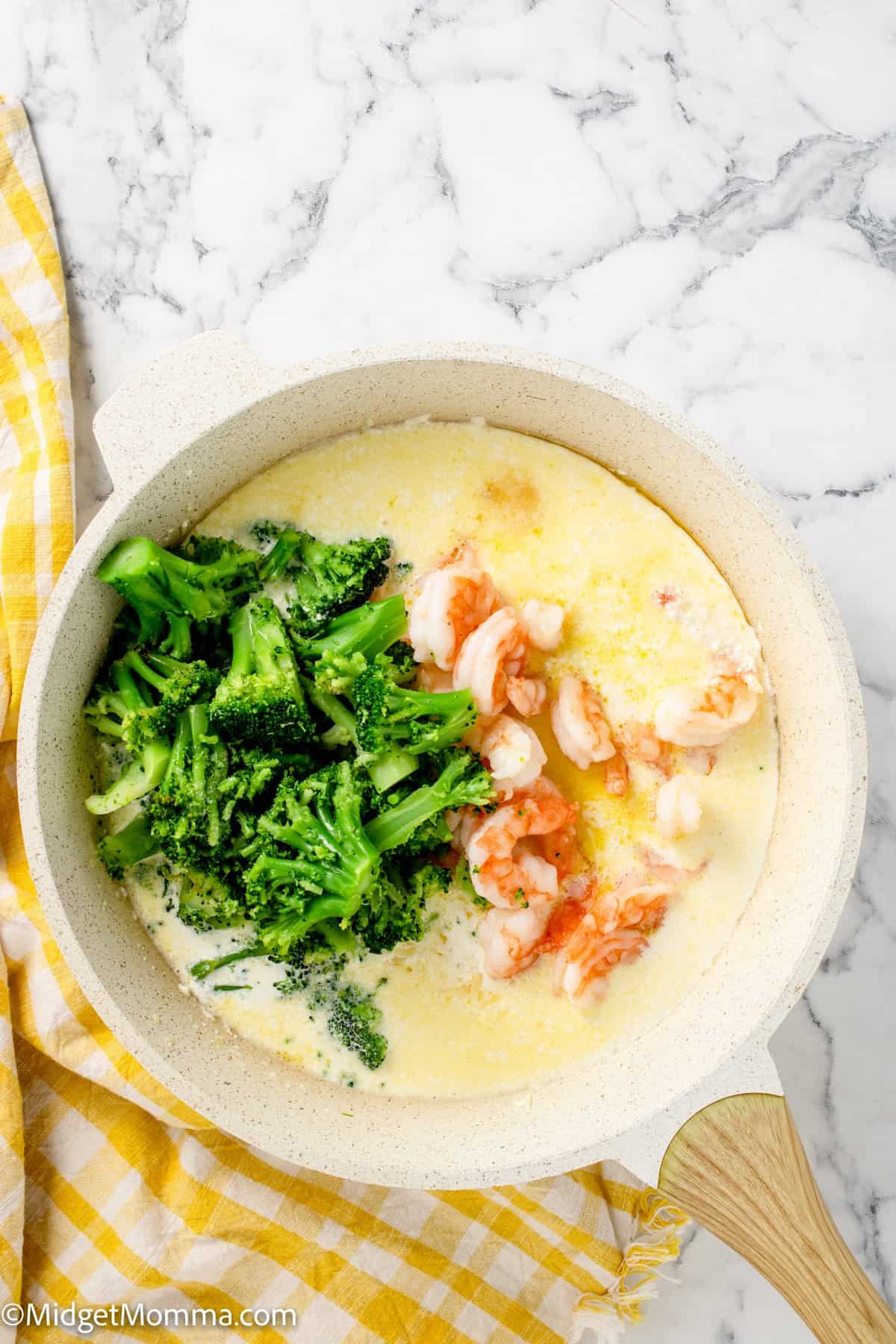 broccoli and shrimp in a skillet of alfredo sauce