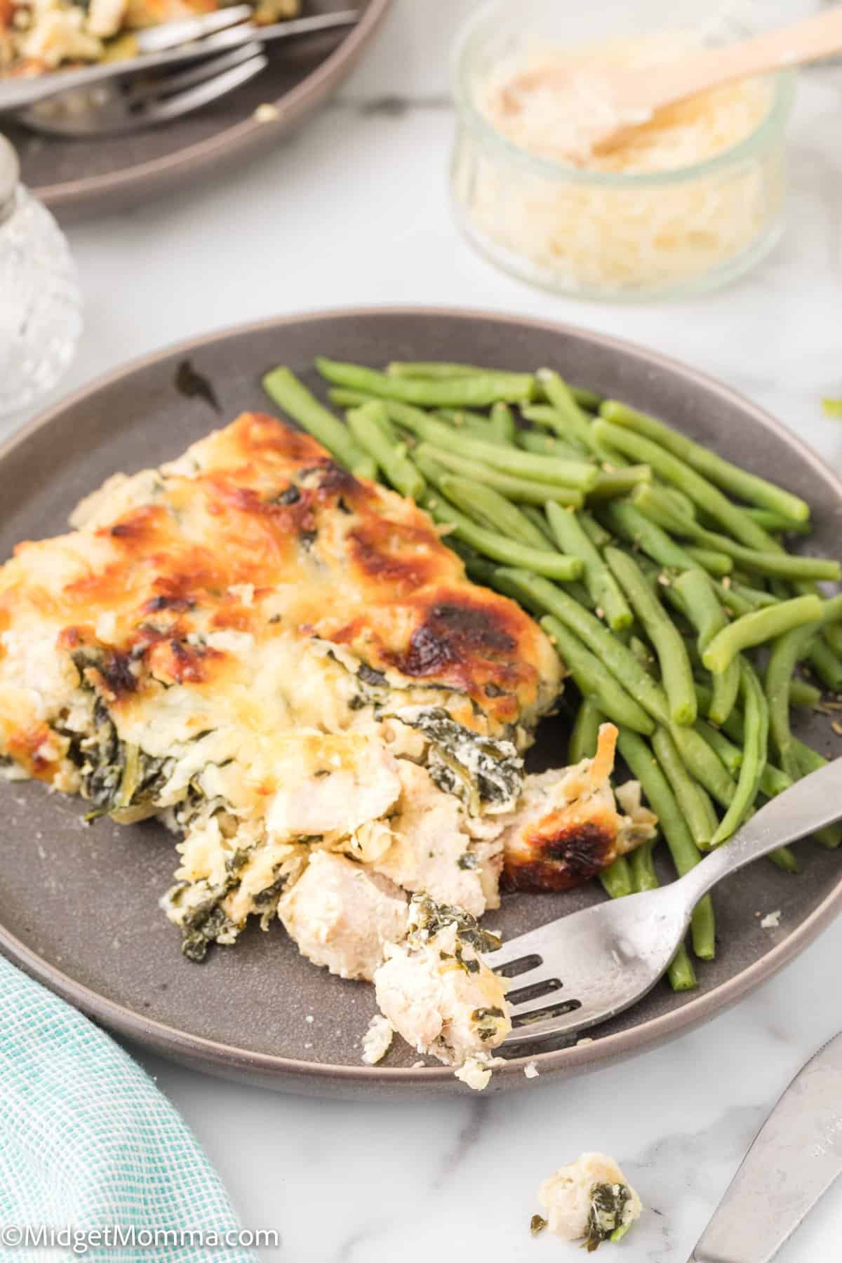 close up photo of a serving of Spinach Artichoke Chicken Casserole with green beans as a side dish on a grey plate