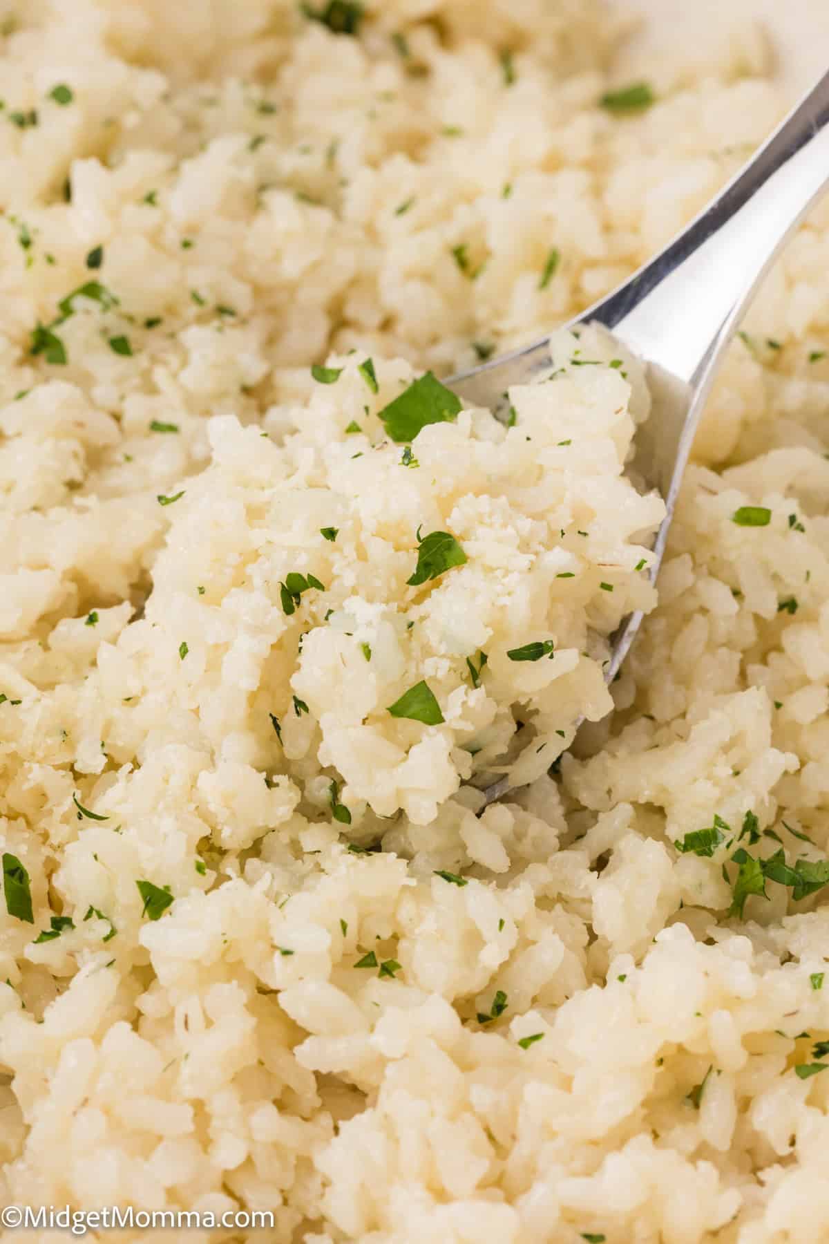 A close-up image of parmesan garlic rice garnished with chopped parsley, with a fork partially in it.