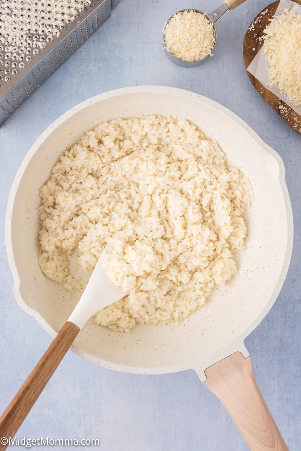 A skillet containing cooked rice with a wooden spoon, on a light blue background.